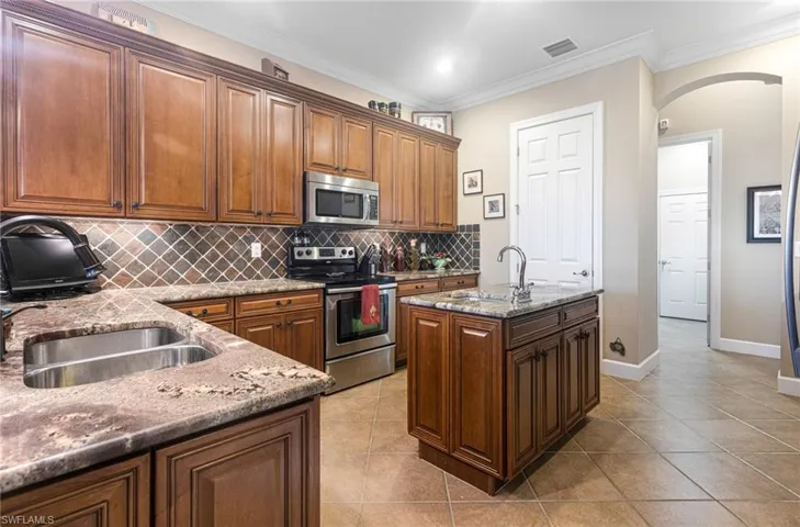 Kitchen featuring visible vents, light stone counters, backsplash, arched walkways, and appliances with stainless steel finishes