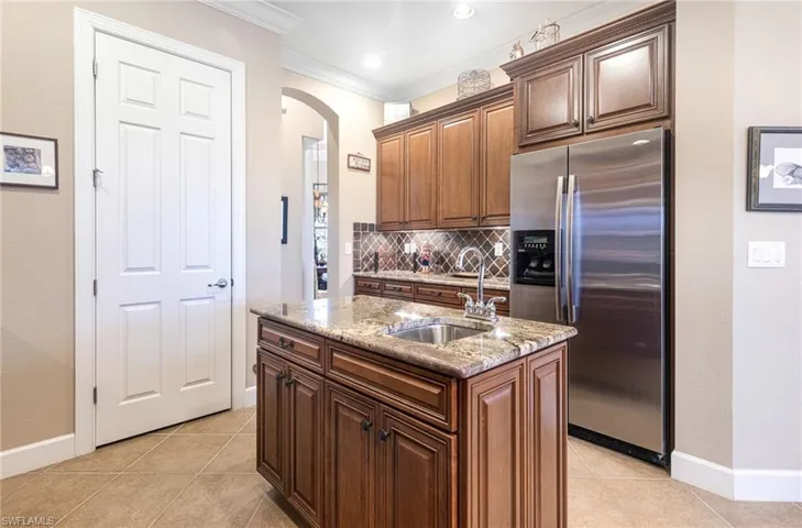 Kitchen featuring ornamental molding, a sink, stainless steel fridge, arched walkways, and light tile patterned flooring
