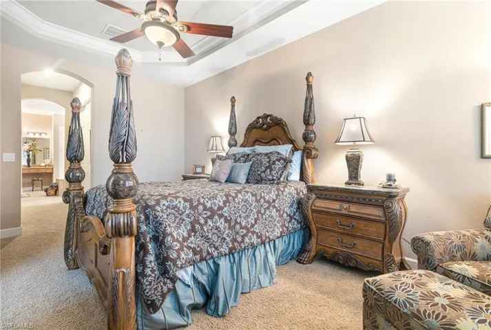 Bedroom featuring visible vents, a tray ceiling, arched walkways, ornamental molding, and light colored carpet
