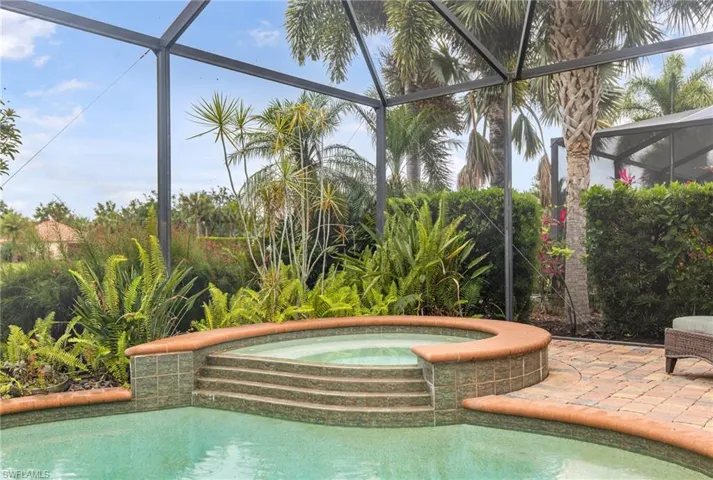 View of swimming pool featuring glass enclosure, a pool with connected hot tub, and a patio