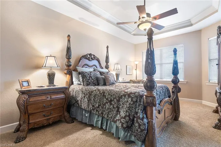 Bedroom featuring a ceiling fan, baseboards, crown molding, a raised ceiling, and light colored carpet