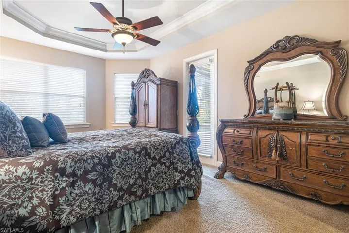 Carpeted bedroom featuring access to outside, a raised ceiling, ceiling fan, and ornamental molding