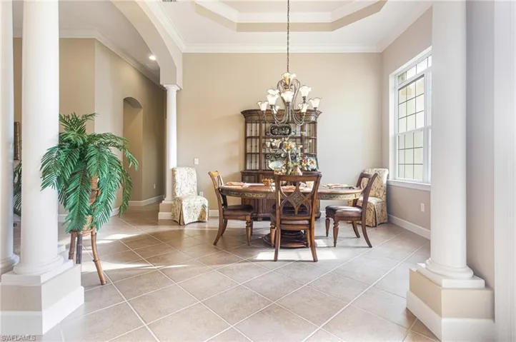 Dining space with light tile patterned floors, ornamental molding, a raised ceiling, and decorative columns