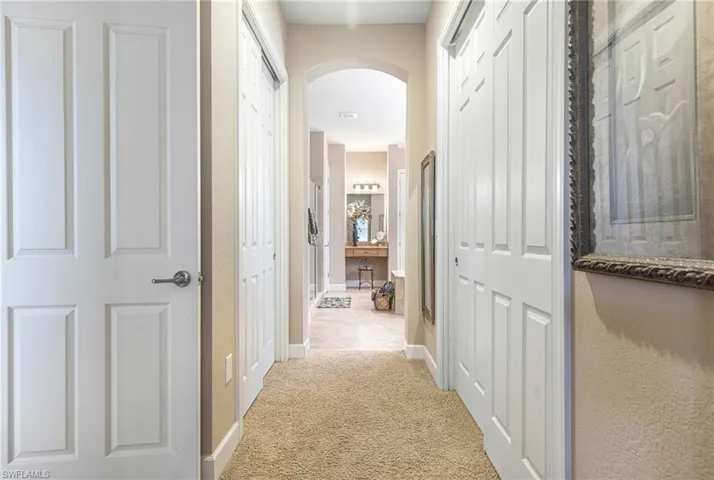 Hall featuring arched walkways, light carpet, and baseboards