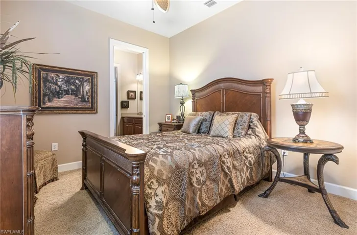 Bedroom with ceiling fan, baseboards, light colored carpet, and ensuite bath