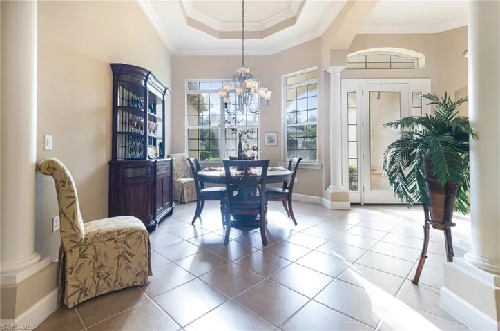 Tiled dining area featuring a notable chandelier, baseboards, crown molding, decorative columns, and a raised ceiling