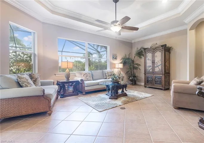 Tiled living room with a tray ceiling, a ceiling fan, arched walkways, and ornamental molding