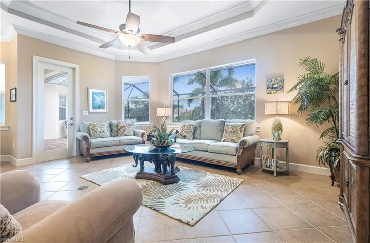 Tiled living area featuring baseboards, a raised ceiling, ceiling fan, and crown molding