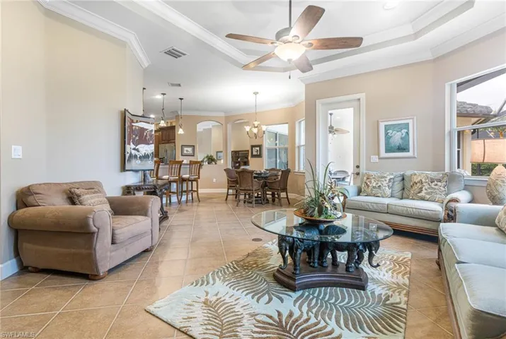 Living area with a tray ceiling, light tile patterned flooring, ceiling fan with notable chandelier, and ornamental molding