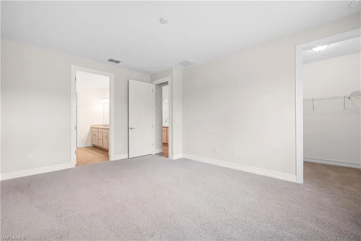 Unfurnished bedroom with a spacious closet, ensuite bathroom, a closet, and light carpet