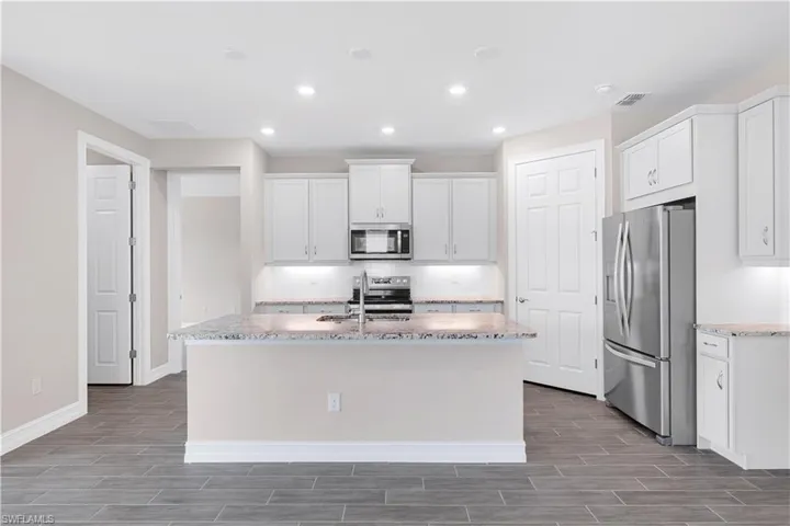 Kitchen featuring backsplash, white cabinetry, sink, a center island with sink, and stainless steel appliances