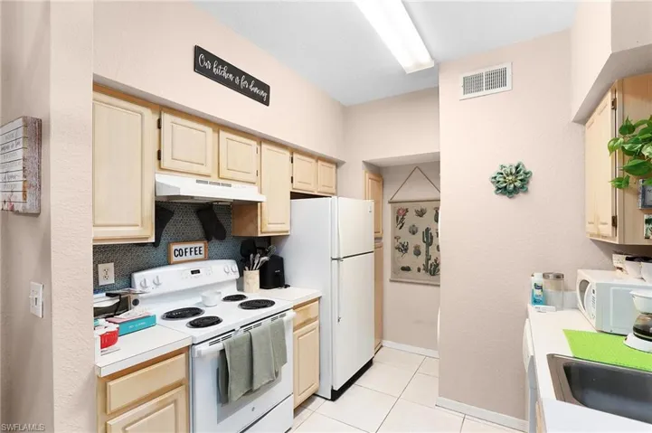 Kitchen with light tile floors, light brown cabinets, sink, and white appliances
