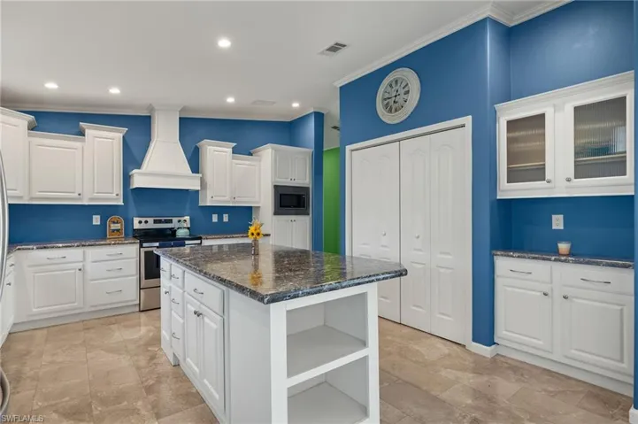 Kitchen with white cabinets, a center island, custom range hood, and stainless steel appliances