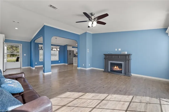 Living room with ceiling fan with notable chandelier, wood-type flooring, and crown molding
