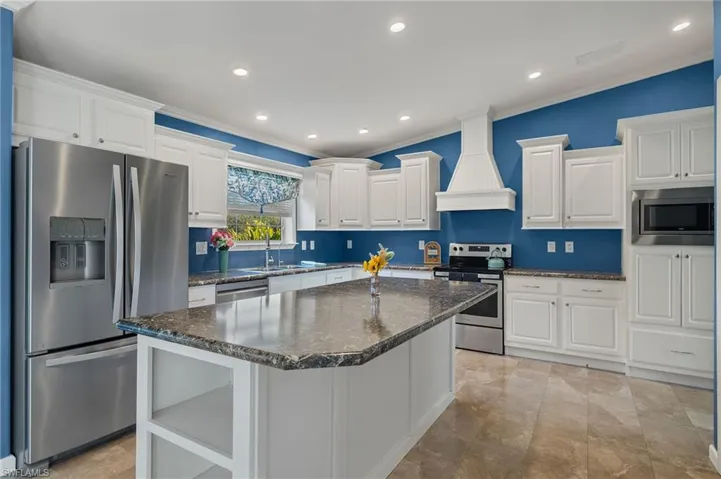 Kitchen with appliances with stainless steel finishes, ornamental molding, custom exhaust hood, a center island, and white cabinetry