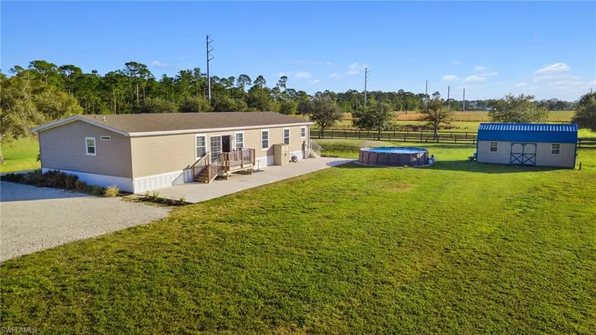 Back of property with a lawn, a rural view, an outdoor structure, and a fenced in pool