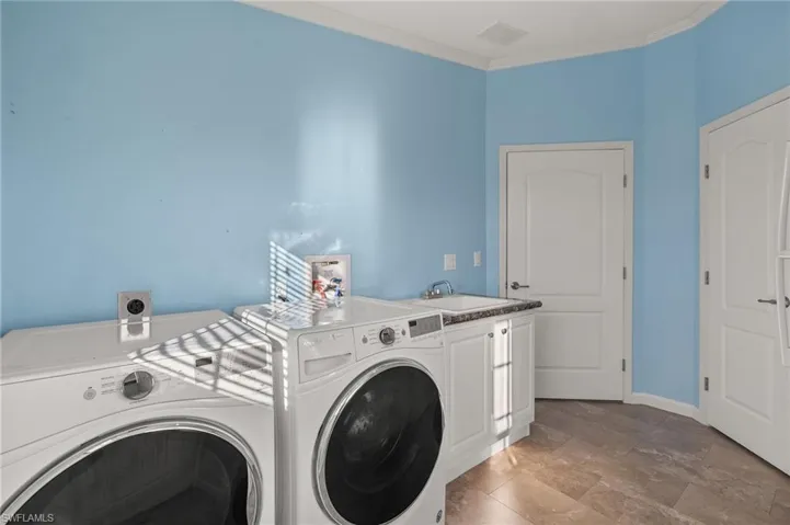 Washroom featuring cabinets, crown molding, washer and dryer, and sink