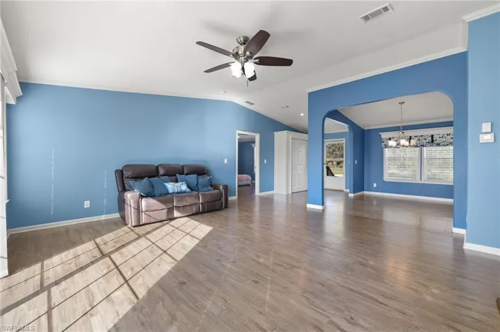 Unfurnished living room with wood-type flooring, ceiling fan with notable chandelier, lofted ceiling, and ornamental molding