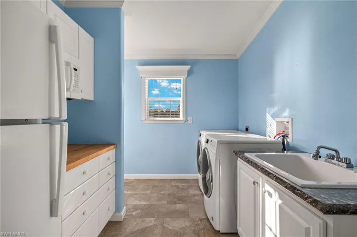 Clothes washing area featuring cabinets, sink, crown molding, and washing machine and dryer