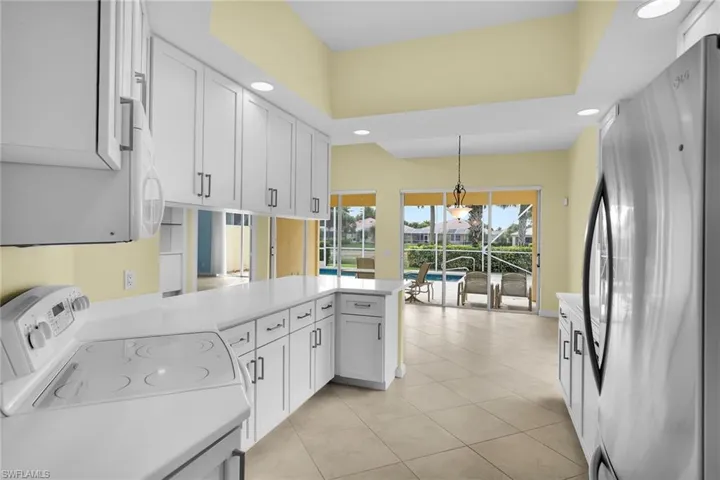 Kitchen featuring white appliances, a peninsula, white cabinetry, light countertops, and pendant lighting