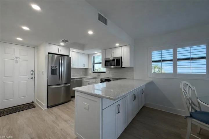 Kitchen featuring stainless steel appliances, light stone countertops, dark wood-style floors, a peninsula, and white cabinets