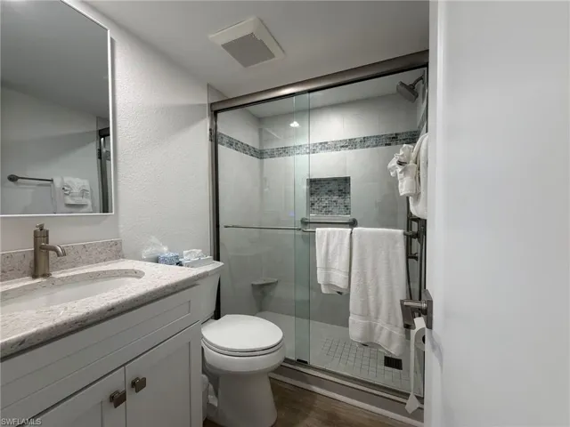 Bathroom featuring a textured wall, vanity, a stall shower, and dark wood-style floors