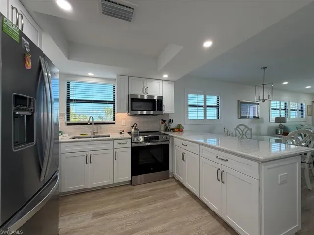 Kitchen with stainless steel appliances, a peninsula, light stone counters, light wood-style floors, and backsplash