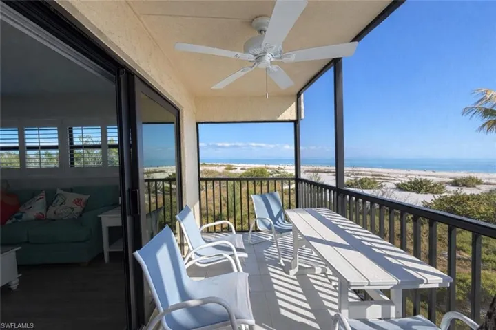 Balcony featuring view of water and beach, a ceiling fan, and outdoor dining space