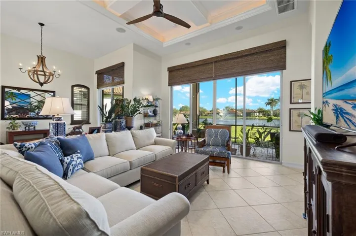 Living room with coffered ceiling, crown molding, a towering ceiling, light tile patterned floors, and ceiling fan with notable chandelier