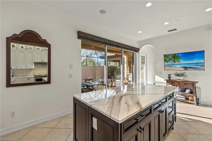 Kitchen with a kitchen island, tasteful backsplash, light stone counters, dark brown cabinets, and light tile patterned floors