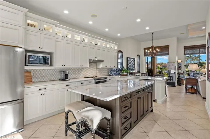 Kitchen with pendant lighting, appliances with stainless steel finishes, a kitchen island, light stone counters, and white cabinetry