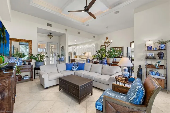 Tiled living room featuring french doors, coffered ceiling, ceiling fan with notable chandelier, crown molding, and beamed ceiling