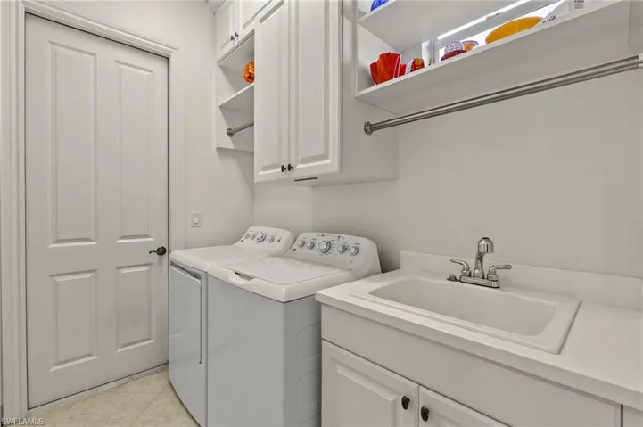 Clothes washing area featuring cabinets, light tile patterned flooring, washer and dryer, and sink