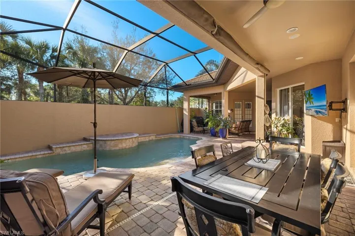 View of swimming pool featuring ceiling fan, a patio, glass enclosure, and a hot tub