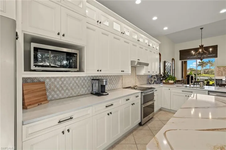 Kitchen with hanging light fixtures, light stone countertops, appliances with stainless steel finishes, light tile patterned flooring, and white cabinetry