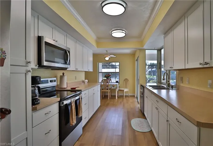 Kitchen featuring sink, a tray ceiling, white cabinets, and appliances with stainless steel finishes
