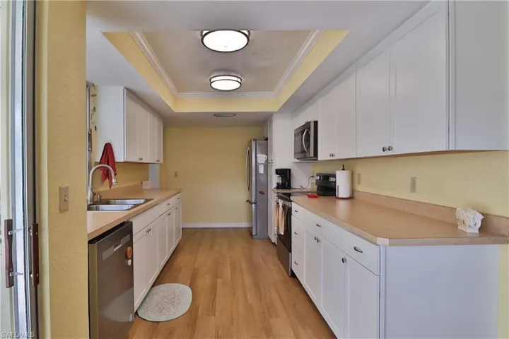 Kitchen featuring stainless steel appliances, a tray ceiling, sink, and white cabinets