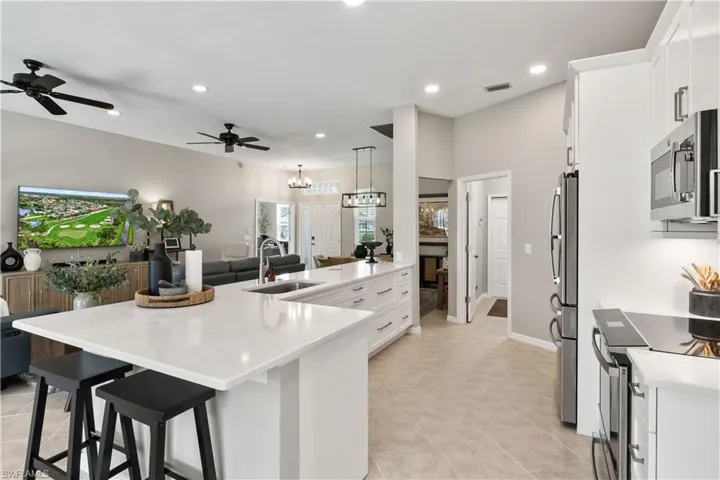 Kitchen featuring appliances with stainless steel finishes, ceiling fan with notable chandelier, white cabinetry, sink, and pendant lighting