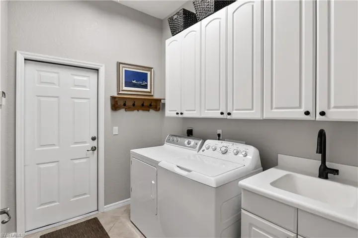 Clothes washing area featuring light tile patterned floors, cabinets, washing machine and dryer, and sink