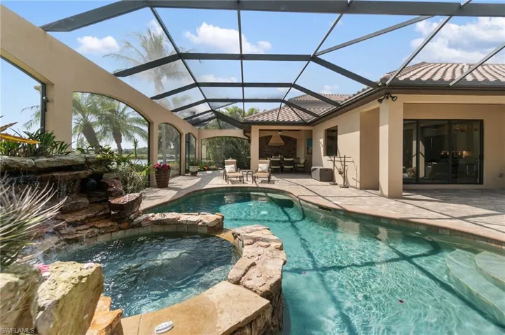 Screened outdoor living area featuring a swimming pool, integrated spa with rock waterfall, covered patio, outdoor dining space, and direct access to interior rooms