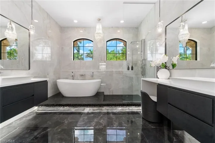 Contemporary bathroom featuring a freestanding tub, dual floating vanities with vessel sinks, a glass-enclosed shower, and arched windows