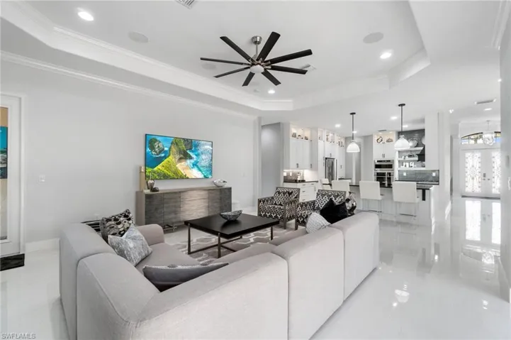 Open-concept living space featuring high-gloss flooring, tray ceilings with recessed lighting, and a modern ceiling fan