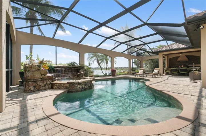 Screened lanai featuring a curved swimming pool with integrated spa and rock waterfall