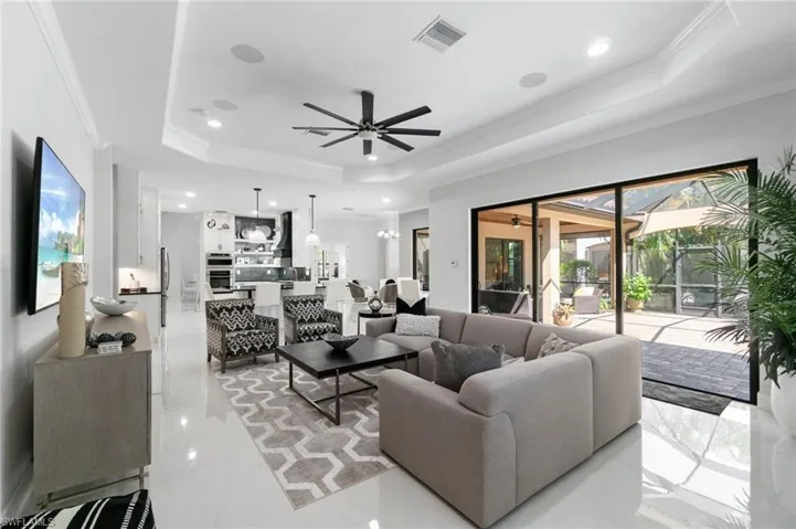Spacious living area featuring polished tile flooring, tray ceilings with recessed lighting, and a modern ceiling fan
