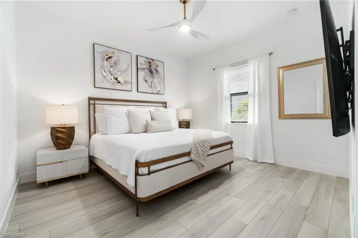 Bright interior space featuring light wood-finish flooring, a ceiling fan with integrated lighting, and a single window with blinds and sheer curtains