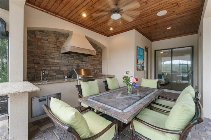 Outdoor kitchen featuring stone veneer backsplash, granite countertops, stainless steel grill, and built-in sink