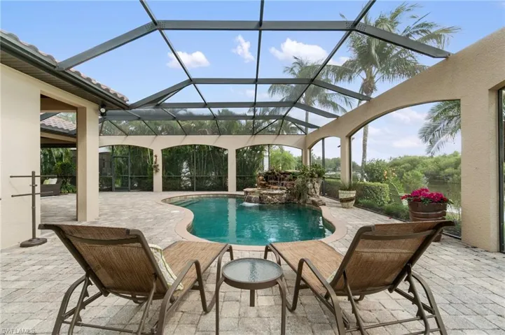 Screened outdoor living area featuring a freeform swimming pool with rock waterfall feature