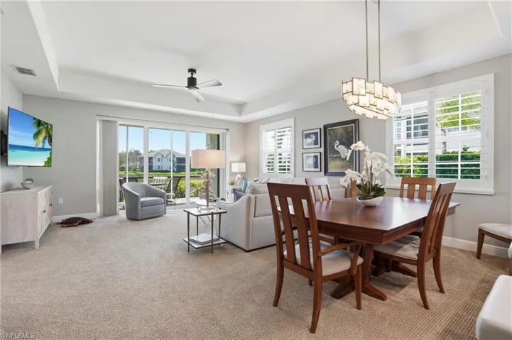 Dining area with a raised ceiling, ceiling fan, and light colored carpet