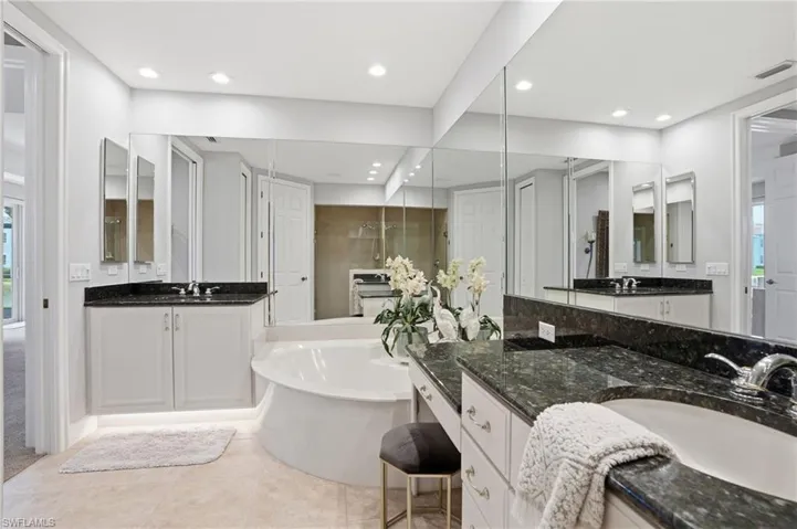 Full bathroom featuring two vanities, light tile patterned floors, a tub, and a closet