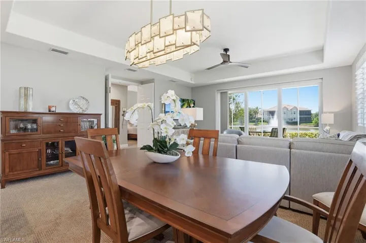 Dining area with a raised ceiling, light carpet, and ceiling fan